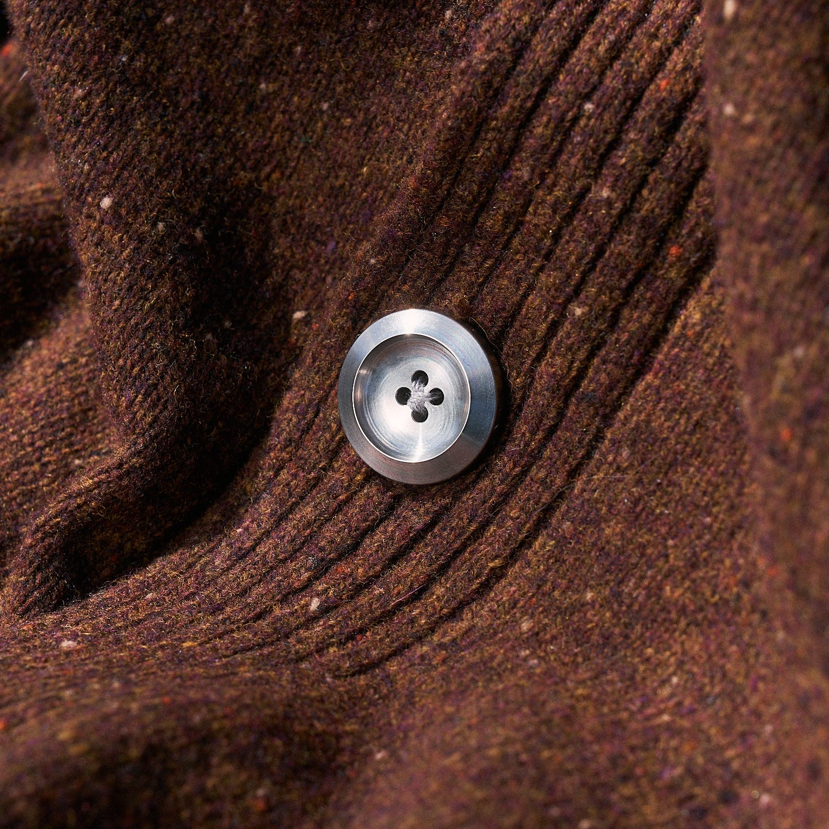 Close-up of a brown textured fabric with a silver button featuring four holes.