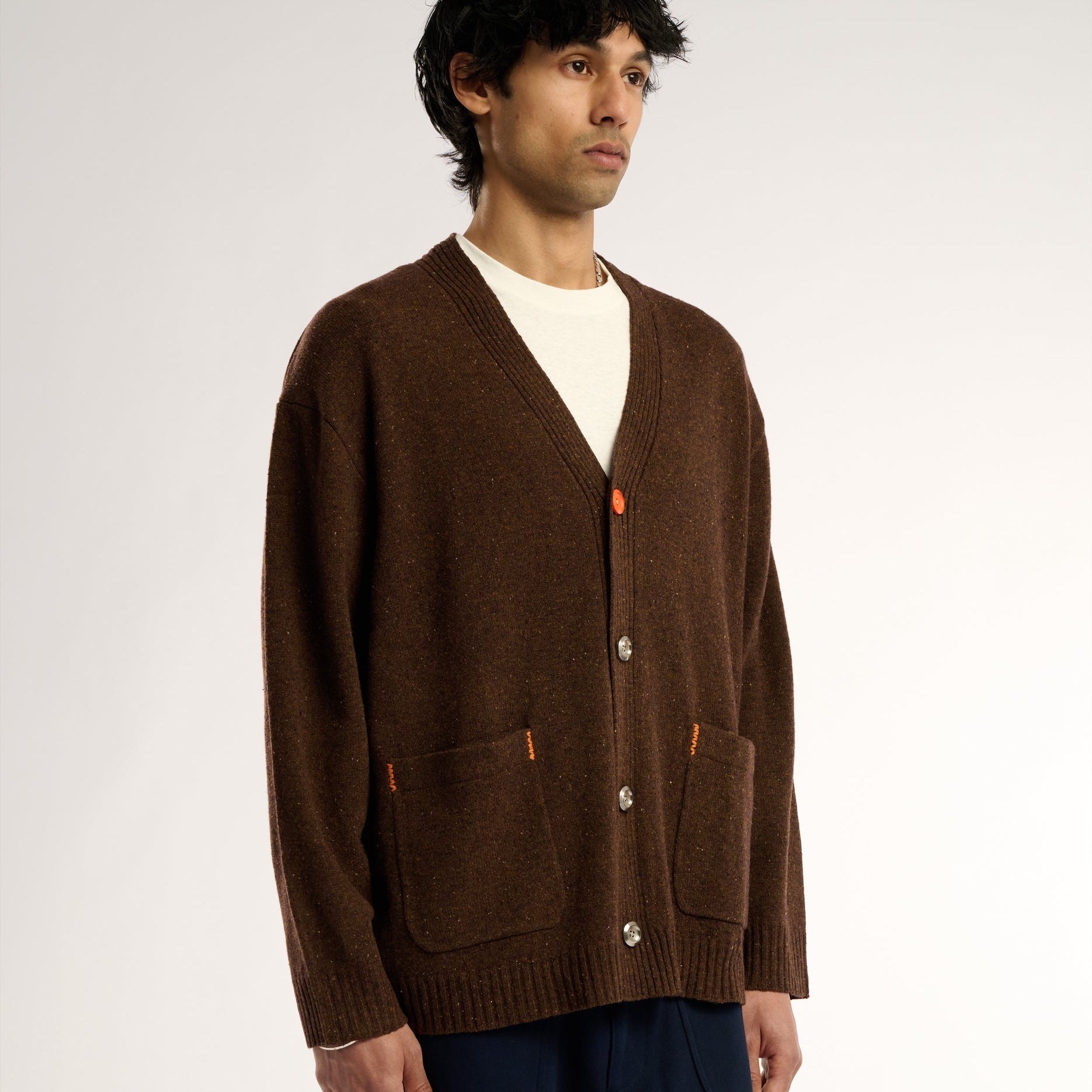 Man wearing a brown cardigan over a white shirt on a plain background