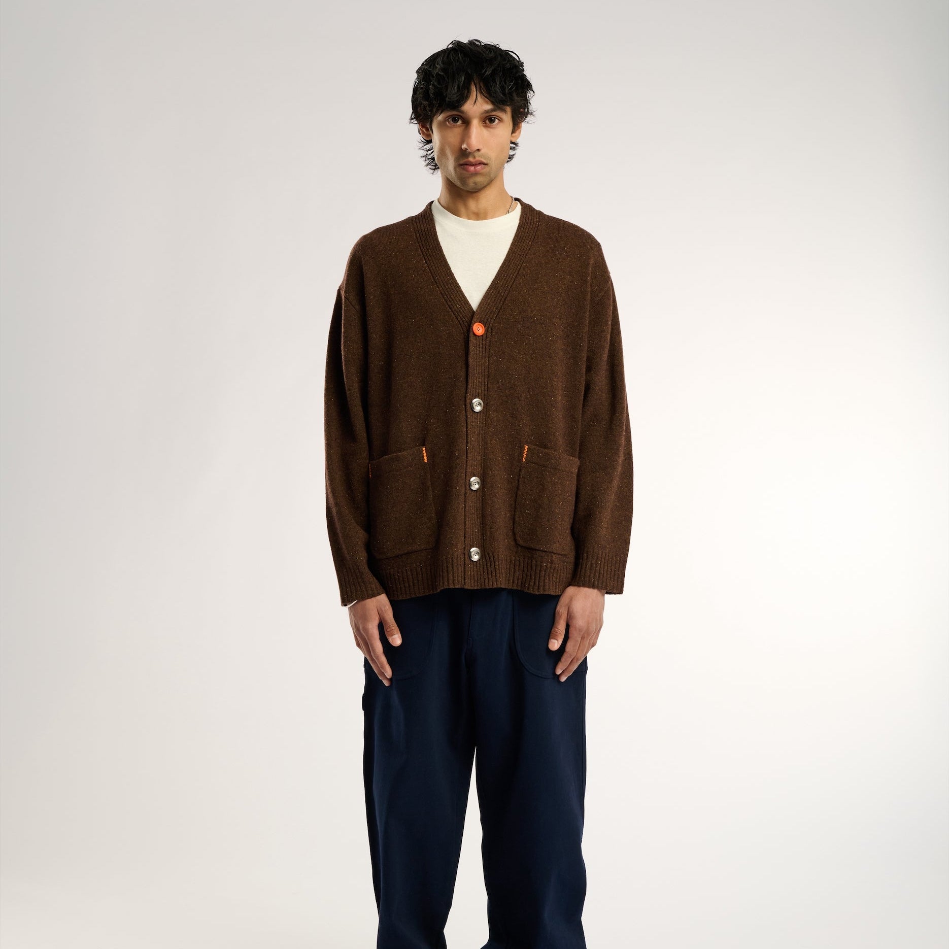 Man wearing a brown cardigan and dark pants on a white background